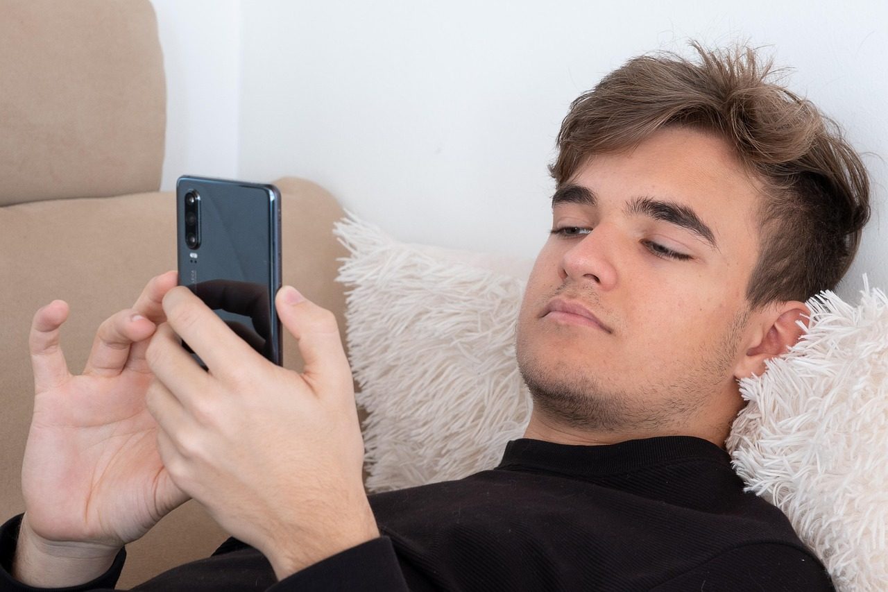 Jugendlicher entspannt mit dem Smartphone auf dem Sofa